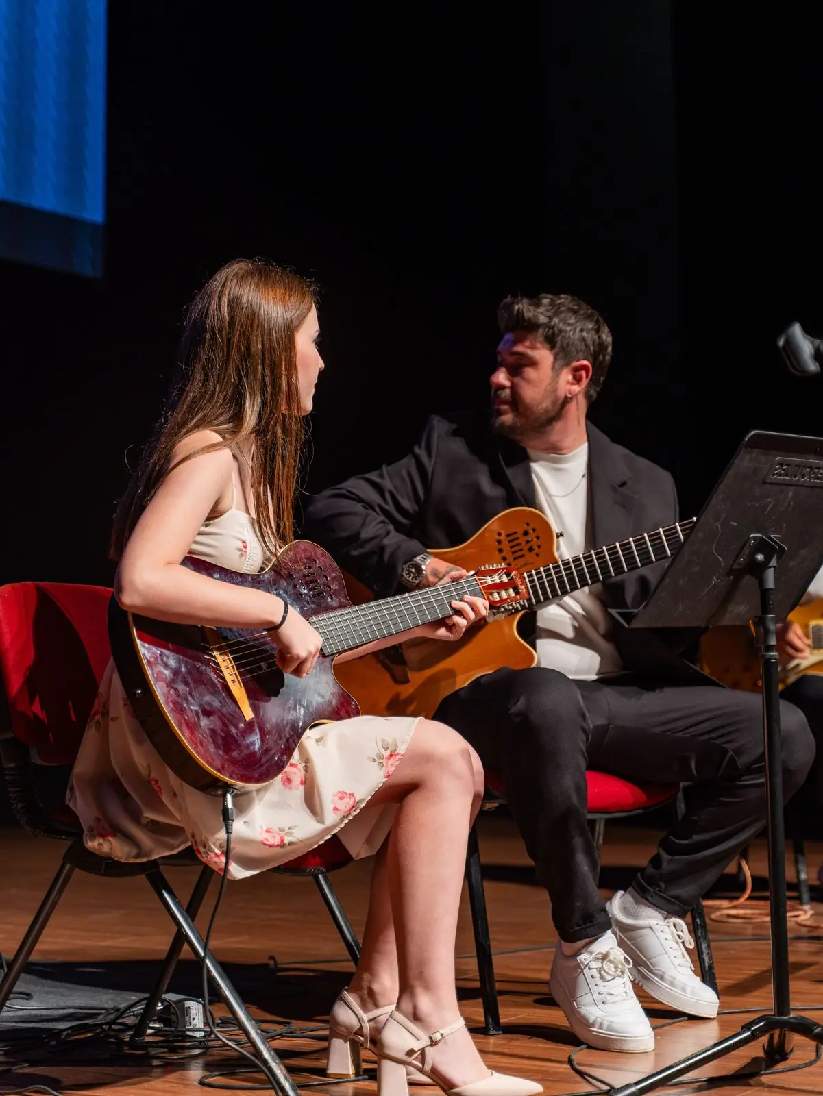 Eğitmen eşliğinde gitar çalan genç öğrenci